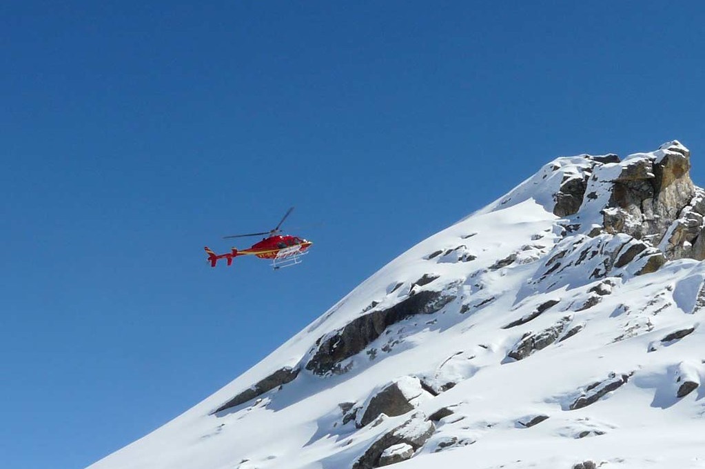 A helicopter reaching the peak of a snowy mountain